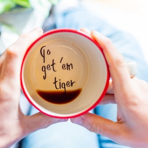 May include: A red coffee mug with the words "Go get 'em tiger" written on the inside. The mug is filled with coffee.