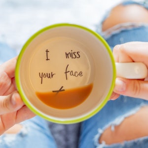 May include: A green and white mug with the words "I miss your face" written on the inside. The mug is filled with coffee.