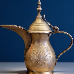 May include: A white ceramic mug with a black handle and the text "But First, Coffee" in a black, handwritten-style font. The mug is on a white surface.