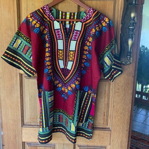 May include: A red, blue, yellow and black patterned dashiki shirt with short sleeves and a V-neck.