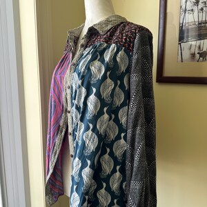 May include: A long-sleeved button-up shirt with a patchwork design. The shirt is made of different fabrics with various patterns, including a teal fabric with white bird silhouettes, a black fabric with white polka dots, and a purple and pink fabric with a wavy pattern.
