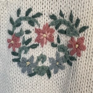 May include: White knitted sweater with embroidered floral design in pink, green and blue.