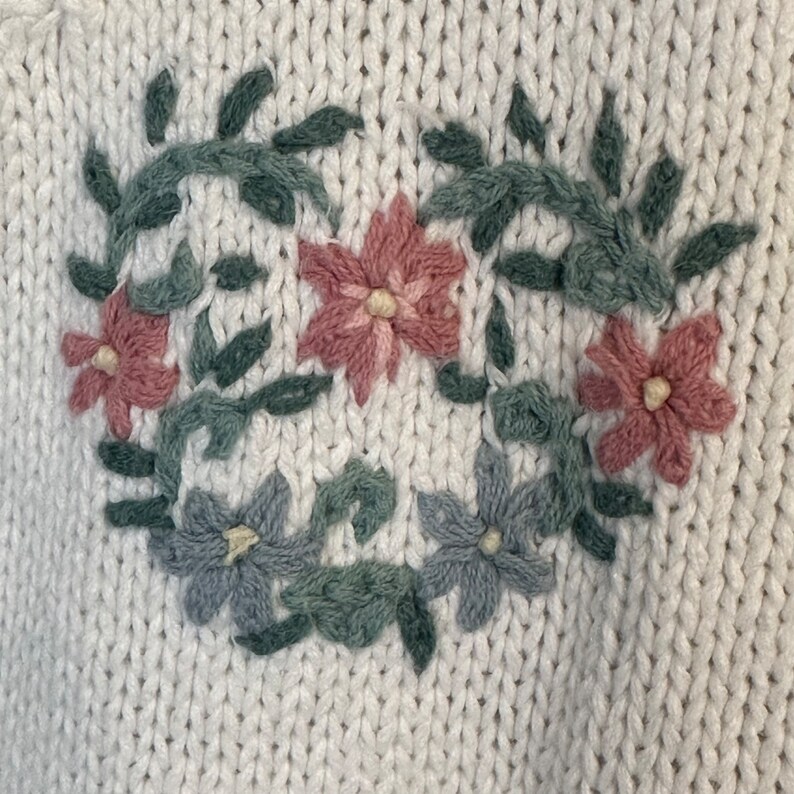 May include: White knitted sweater with embroidered floral design in pink, green and blue.