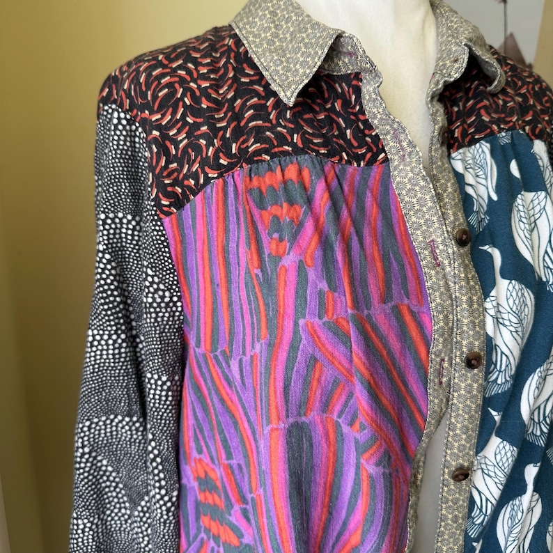 May include: A long-sleeved shirt with a patchwork design. The shirt is made of different fabrics with various patterns, including black and white polka dots, red and black swirls, purple and pink stripes, and blue and white birds. The shirt has a button-up front and a collar.