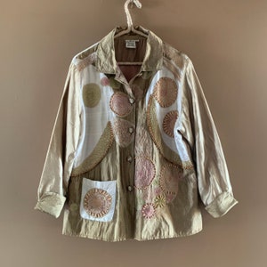 May include: A beige button-up jacket with a white lining and embroidered circles in shades of brown, pink, and green.