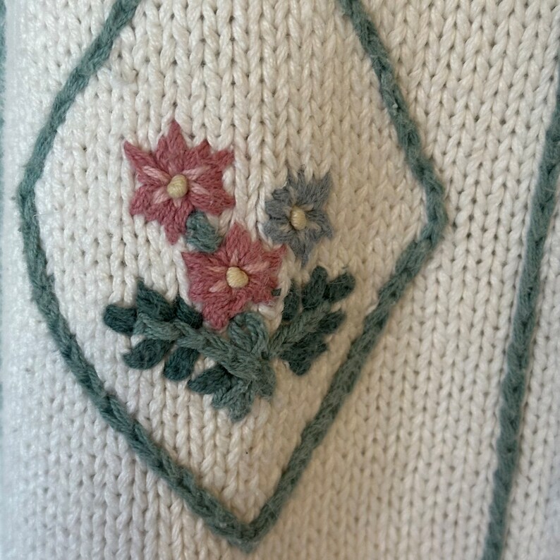 May include: White knitted fabric with a green diamond shape embroidered with pink and blue flowers.