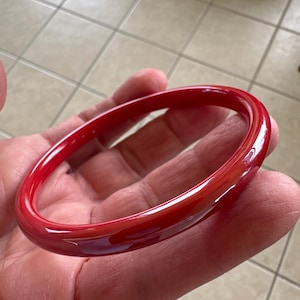 May include: A bright red bangle bracelet made of polished glass. The bracelet is round and smooth.