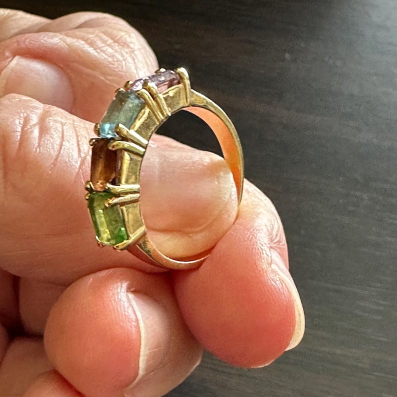 K&ouml;nnte beinhalten: Ein Goldring mit f&uuml;nf rechteckigen Edelsteinen. Die Edelsteine sind gr&uuml;n, braun, blau und lila.