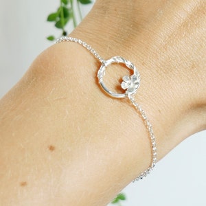 Peut inclure: Un bracelet en argent avec un délicat charme de fleur et un design de cercle torsadé.