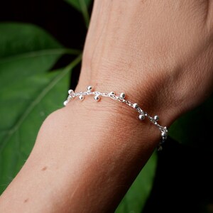 Pode incluir: Um bracelete de corrente de prata com pequenas contas redondas. O bracelete est&aacute; no pulso de uma pessoa.