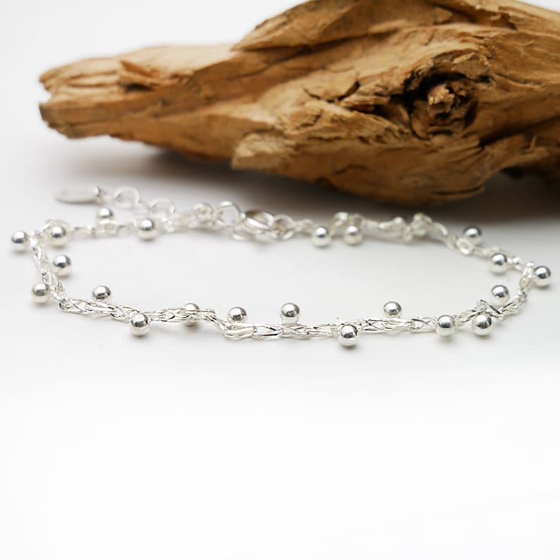 Pode incluir: Um delicado bracelete de corrente de prata com pequenas contas de prata penduradas na corrente.