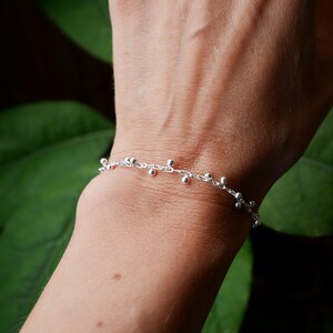 Pode incluir: Um bracelete de corrente de prata com pequenas contas de prata penduradas.