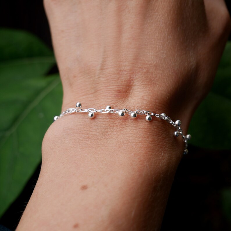 Pode incluir: Um bracelete de corrente de prata com pequenas contas de prata penduradas.