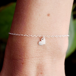 Könnte beinhalten: Ein zartes silbernes Kettenarmband mit einem kleinen Herz-Anhänger.