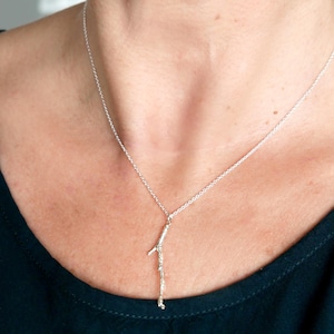 May include: A silver necklace with a delicate twig pendant. The twig is made of sterling silver and has a natural, organic look.