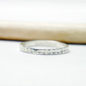 Op de afbeelding: Een zilveren bandring met een getextureerd ontwerp. De ring is simpel en elegant.