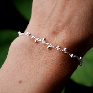 Pode incluir: Um bracelete de corrente de prata com pequenas contas de prata penduradas.