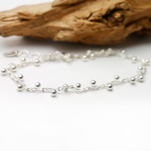 Pode incluir: Um delicado bracelete de corrente de prata com pequenas contas de prata penduradas.