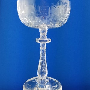 Pode incluir: Uma taça de champanhe transparente com desenhos florais gravados. A taça larga e arredondada assenta numa haste detalhada com um design texturizado. A base também apresenta desenhos florais gravados.