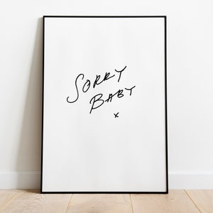 Puede incluir: Una impresi&oacute;n art&iacute;stica enmarcada con las palabras "Sorry Baby" en escritura negra a mano sobre un fondo blanco. La impresi&oacute;n est&aacute; en un marco negro y est&aacute; apoyada contra una pared blanca sobre un suelo de madera.