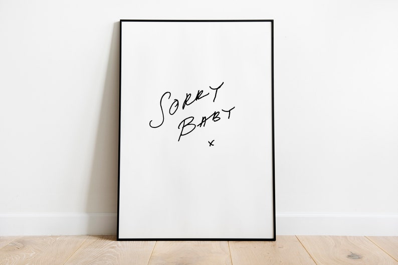 Puede incluir: Una impresi&oacute;n art&iacute;stica enmarcada con las palabras "Sorry Baby" en escritura negra a mano sobre un fondo blanco. La impresi&oacute;n est&aacute; en un marco negro y est&aacute; apoyada contra una pared blanca sobre un suelo de madera.