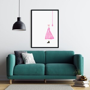 Puede incluir: Una impresi&oacute;n art&iacute;stica enmarcada que presenta una ilustraci&oacute;n de un vestido rosa y un zapato negro. La obra de arte est&aacute; sobre un fondo blanco. La habitaci&oacute;n incluye un sof&aacute; turquesa, almohadas, una l&aacute;mpara colgante negra y una pila de libros.
