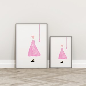 Puede incluir: Dos impresiones art&iacute;sticas enmarcadas. Cada impresi&oacute;n presenta una ilustraci&oacute;n en acuarela rosa de una figura con un vestido rosa y botas negras con detalles amarillos. Una l&iacute;nea rosa y una forma de l&aacute;grima est&aacute;n encima de la figura. Marcos negros.