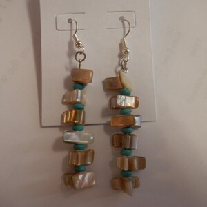 May include: Dangling earrings with a silver hook, featuring a vertical arrangement of rectangular, iridescent shell pieces and small turquoise beads. The earrings are displayed on a white card.