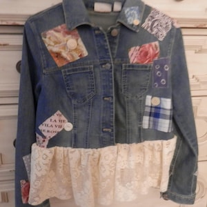 May include: A blue denim jacket with a lace trim and various fabric patches, including a plaid patch, a floral patch, and a patch with the text "La Vie Vila Vie Serons".