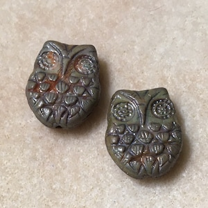 May include: Two ceramic owl beads with a green glaze and brown accents. The owls have detailed eyes and feathers.