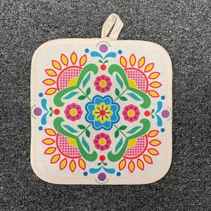 May include: Square, off-white pot holder with a colorful floral design. The design features pink, yellow, green, and blue flowers arranged in a symmetrical pattern. A small loop is attached for hanging.