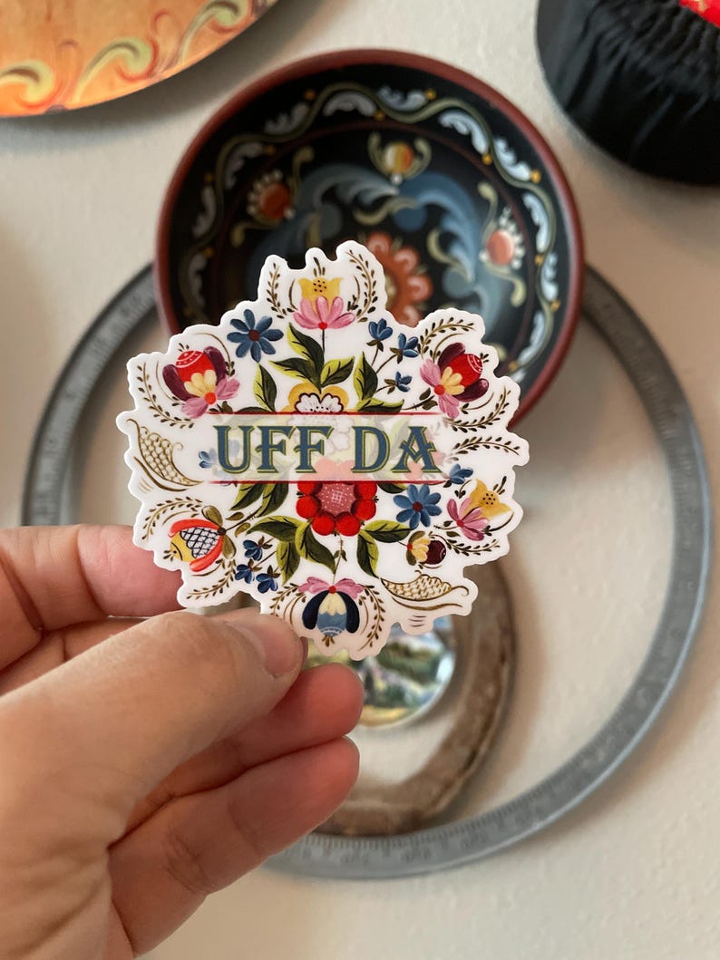 diecut adhesive sticker features colorful Norwegian rosemaling with the phrase ‘Uff Da’ written across the center