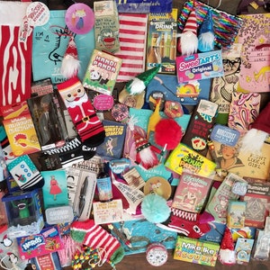 May include: A collection of colorful and whimsical gifts, including socks, ornaments, bath products, and small toys. The items are arranged on a wooden surface and feature a variety of themes, such as Christmas, gnomes, and animals.