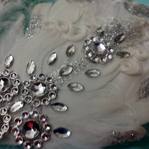 Pu&ograve; includere: Fascia per capelli in piume bianche con glitter argentati e strass. La fascia &egrave; decorata con un grande gruppo di strass al centro e strass pi&ugrave; piccoli sparsi su tutta la superficie.