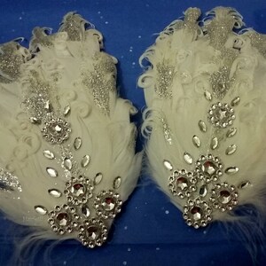 Pu&ograve; includere: Due fermagli per capelli in piume bianche con glitter argentati e strass. I fermagli sono decorati con un gruppo di strass al centro.