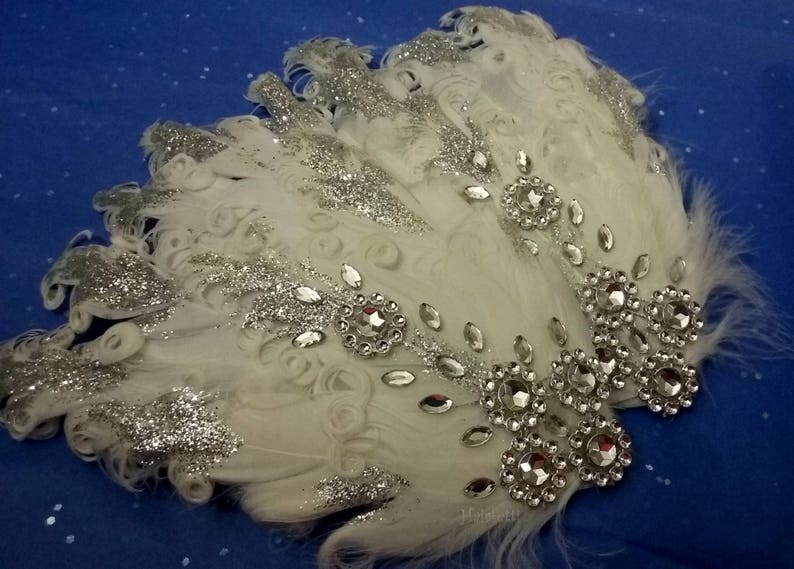 Pu&ograve; includere: Pettine per capelli in piume bianche con glitter argentato e strass. Il pettine &egrave; decorato con un gruppo di grandi strass al centro e strass pi&ugrave; piccoli sui bordi.