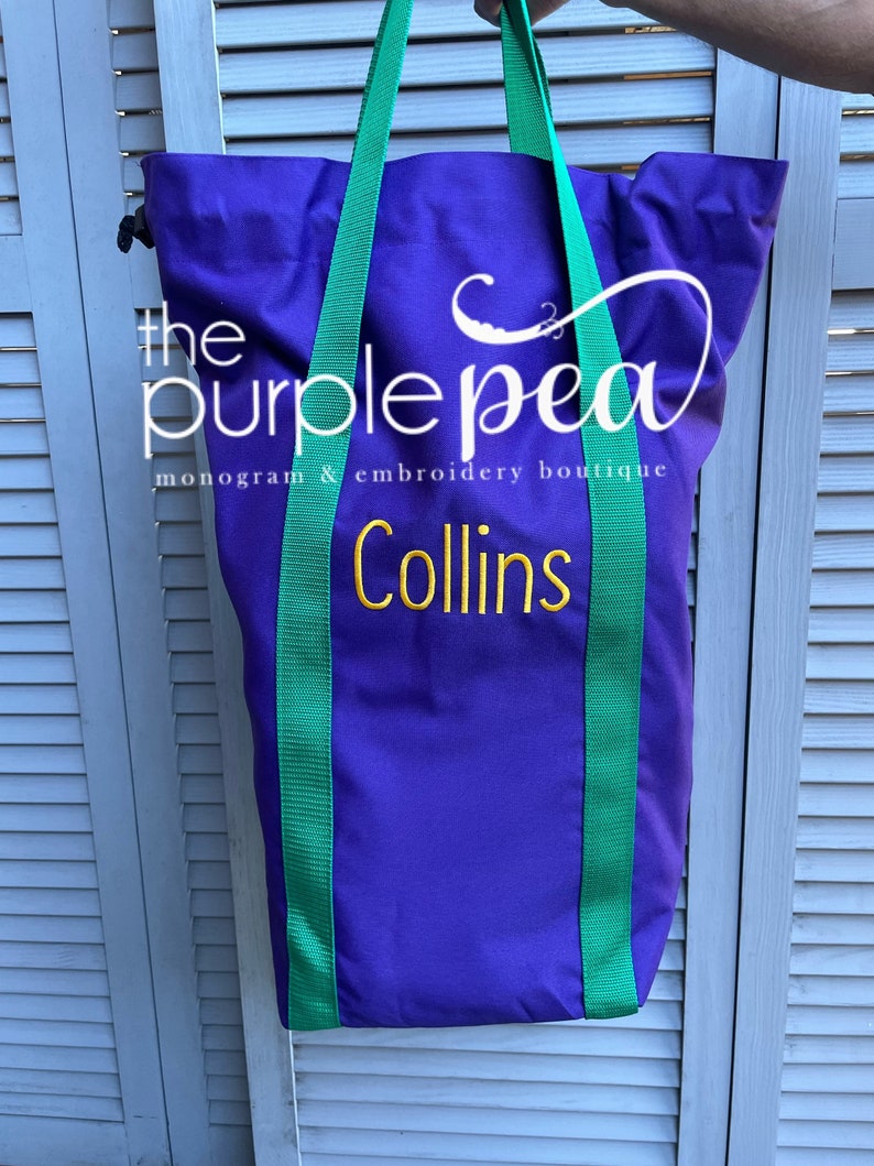 Puede incluir: Bolsa de lona morada con correas verdes y el texto "the purple pea monogram & embroidery boutique Collins" bordado en dorado.
