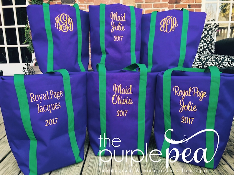 Puede incluir: Seis bolsas de mano de color morado con correas verdes. Cada bolsa tiene un dise&ntilde;o bordado diferente, incluyendo nombres, monogramas y el texto "Royal Page" y "Maid". Las bolsas est&aacute;n dispuestas en una fila sobre una superficie de madera. El texto "the purple pea" es visible en la parte inferior de la imagen.