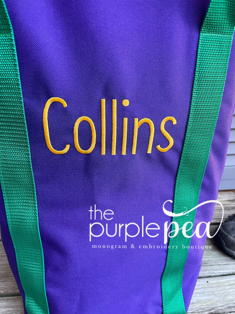 Puede incluir: Bolsa de lona morada con correas verdes y el nombre "Collins" bordado en amarillo. La bolsa tiene el texto "the purple pea monogram & embroidery boutique" impreso en la parte inferior.