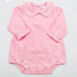 May include: A pink baby onesie with long sleeves and a white scalloped collar. The onesie has a snap closure at the bottom.
