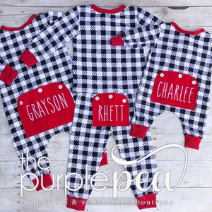 May include: Three black and white buffalo plaid pajamas with red trim and personalized pockets. The pockets are embroidered with the names Grayson, Rhett, and Charlee.