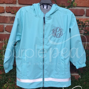 May include: A light blue hooded jacket with a reflective strip at the bottom. The jacket has a zipper closure and a gray monogram on the front. The text "the purple pea monogram & embroidery boutique" is visible at the bottom of the image.