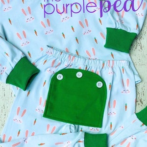 May include: A light blue pajama set with a bunny and carrot print. The set has green trim and a green pocket on the pants. The text "the purple pea" is visible on the top.