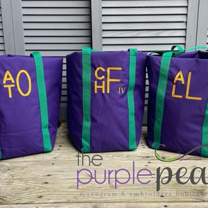 Puede incluir: Tres bolsas de lona moradas con correas verdes y iniciales bordadas en amarillo. Las bolsas est&aacute;n sobre una superficie de madera con el texto "the purple pea monogram & embroidery boutique" debajo.