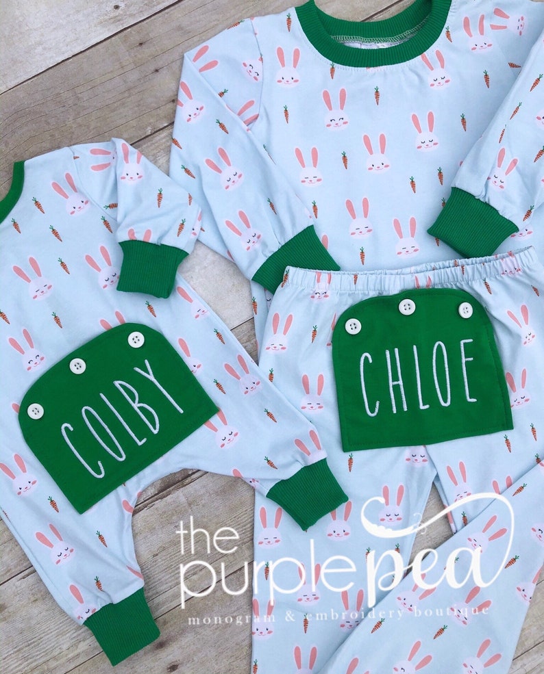 May include: Two pairs of light blue pajamas with a bunny and carrot print. One pair has a green pocket with the name "COLBY" embroidered on it. The other pair has a green pocket with the name "CHLOE" embroidered on it.