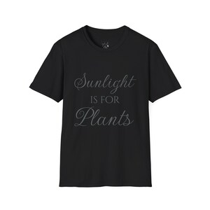 Puede incluir: Camiseta negra de cuello redondo con el texto "Sunlight is for Plants" en fuente cursiva. La camiseta es de color negro liso y tiene mangas cortas. El texto es de color gris claro.