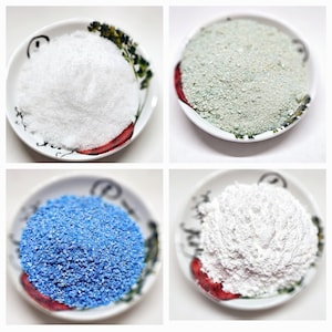 May include: Four small white ceramic dishes with red trim, each containing a different type of white powder. The powders are arranged in a grid pattern, with the top left dish containing a fine white powder, the top right dish containing a coarse white powder, the bottom left dish containing a blue powder, and the bottom right dish containing a white powder.