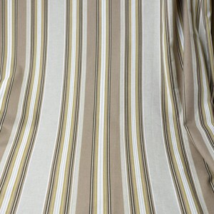 Puede incluir: Tela con rayas verticales en tonos beige, blanco y verde oliva. Las rayas var&iacute;an en ancho, creando una apariencia texturizada. La tela est&aacute; drapeada, lo que sugiere que podr&iacute;a usarse para cortinas o tapicer&iacute;a.