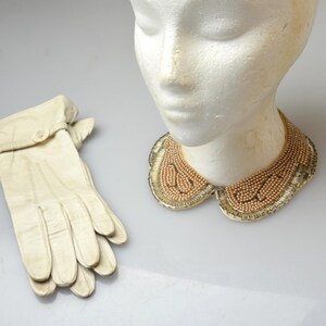 May include: A white mannequin wearing a gold beaded collar, a pair of white leather gloves, and a three-strand pearl necklace with yellow ribbon ties.