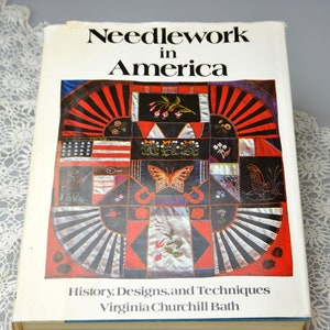 May include: A book titled "Needlework in America: History, Designs, and Techniques" by Virginia Churchill Bath. The cover features a colourful patchwork quilt with a butterfly in the centre.